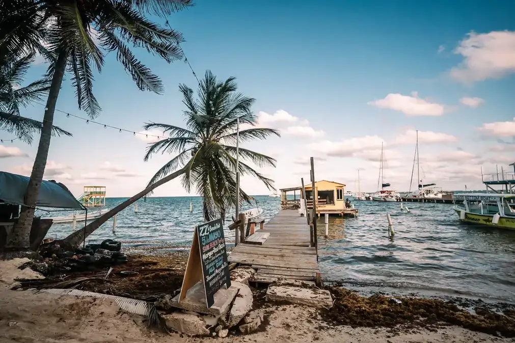 Best eSIM for Belize: a wooden dock, palm trees, and boats on the turquoise water of a Belize caye