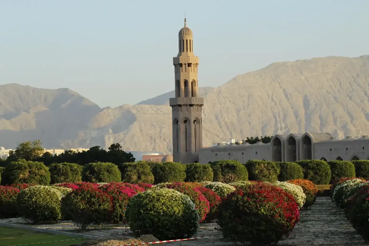 Best eSIM for Oman: a mosque minaret framed by gardens and mountains at sunset near Muscat